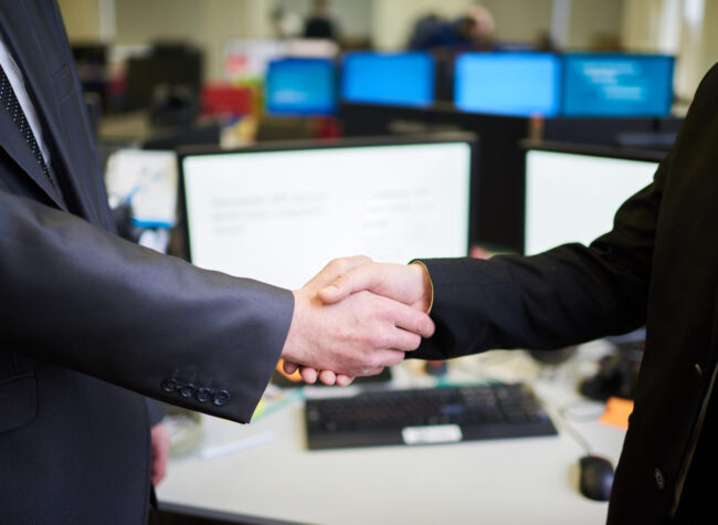 Side view closeup of two unrecognizable business people shaking hands standing in office, copy space